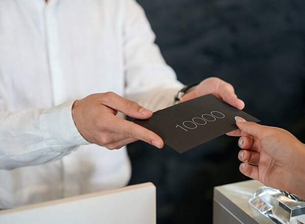 A person hands a black envelope labeled "10000" to another person across a counter.
