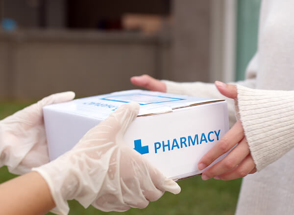 A person wearing gloves hands a white box labeled "Pharmacy" to another person.