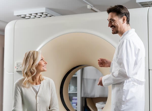 A doctor speaks with a patient who is seated in front of an MRI or CT scanner in a medical facility.