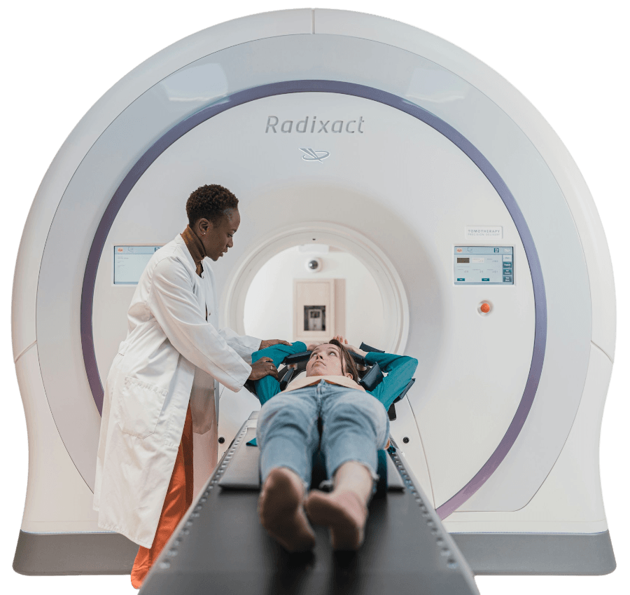 A medical professional assists a patient lying on a table in front of a Radixact imaging machine, preparing for a scan.