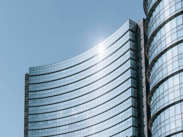 Modern glass office building with curved facade reflecting sunlight against a clear blue sky.