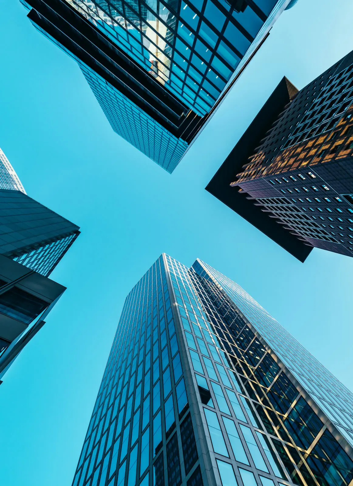 Upward view of tall glass skyscrapers under a clear blue sky.