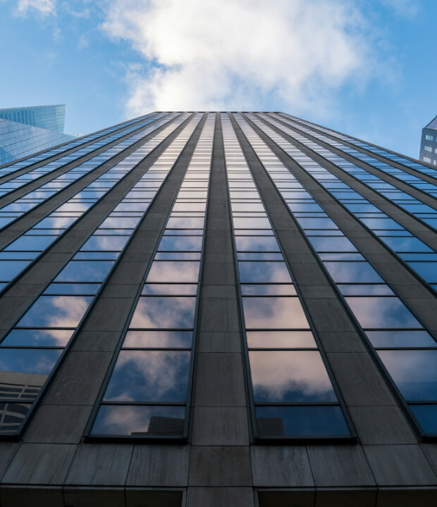 Looking up at a tall, modern skyscraper with reflective glass windows against a blue sky with clouds.