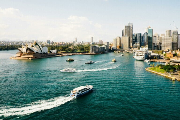 Aerial view of Sydney Harbour with the Opera House and downtown skyline, featuring boats on the water, highlighting Australian human rights issues.