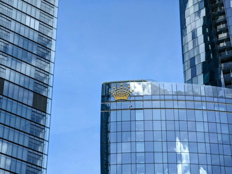 Modern skyscrapers with reflective glass facades under a clear blue sky, one building features a unique gold-patterned section on its curved top amid economic forecasts.