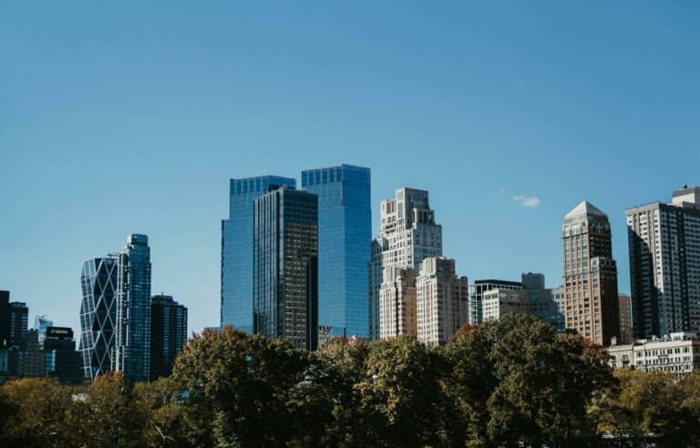 A cityscape showing modern high-rise buildings under a clear blue sky, with lush greenery in the foreground equipped for disability accommodation.