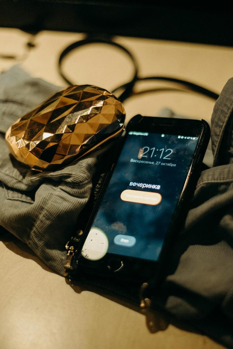 A smartphone displays a call screen with the word "вечеринка" (party) in Russian, lying on fabric next to a gold, faceted object and a black hairband.