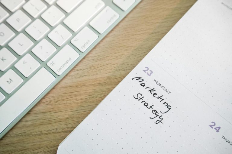 A close-up of a keyboard next to a planner open to Wednesday the 23rd, with "Marketing Strategy" handwritten on that day.