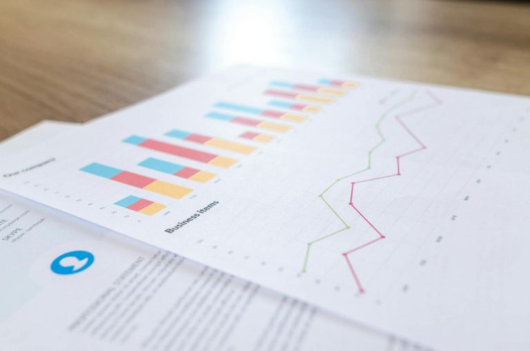 Close-up of printed business reports showing a bar chart and a line graph with various colored data, placed on a wooden surface.