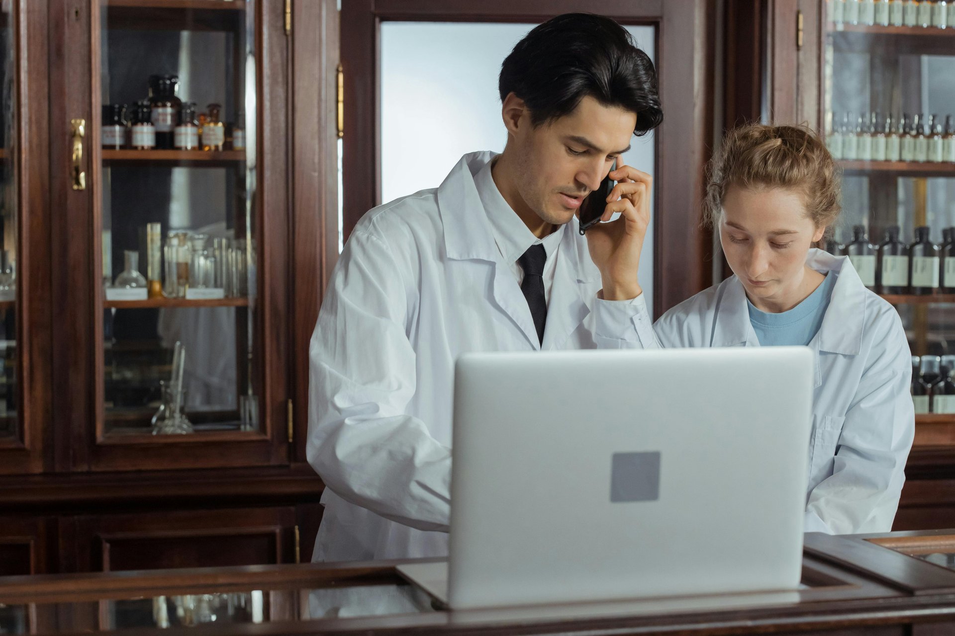 Two healthcare professionals working together in a pharmacy using laptop