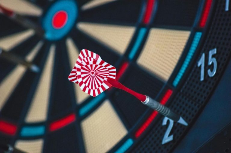 A close-up of a red and white dart stuck in the number 2 section of a dartboard.
