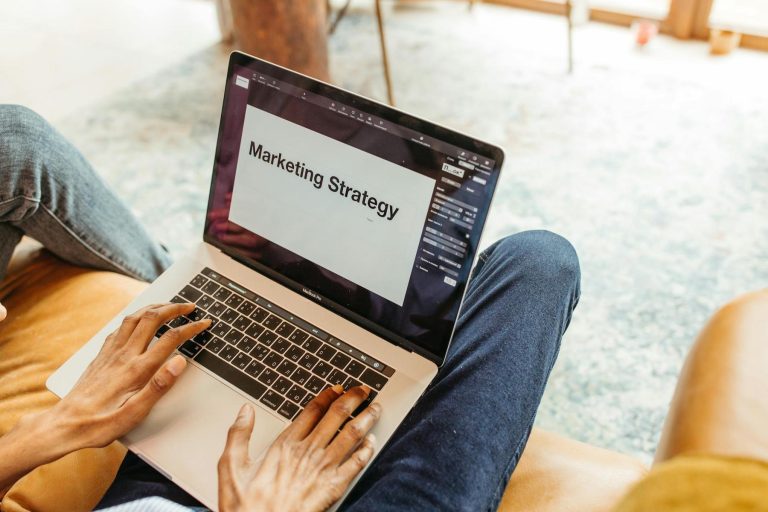 Person sitting on a couch using a laptop displaying a presentation slide with the text "Marketing Strategy.