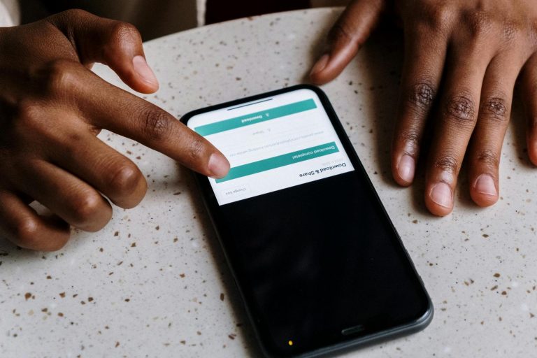 A person uses a smartphone on a speckled table, with a finger tapping the screen displaying a form or menu.