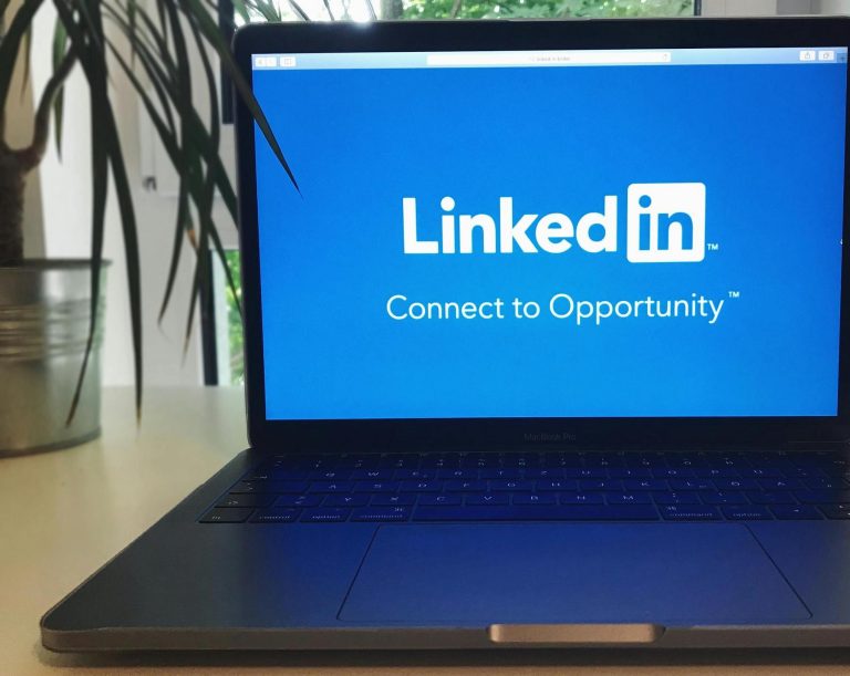 A laptop displays the LinkedIn homepage with the slogan "Connect to Opportunity," positioned on a desk near a potted plant.