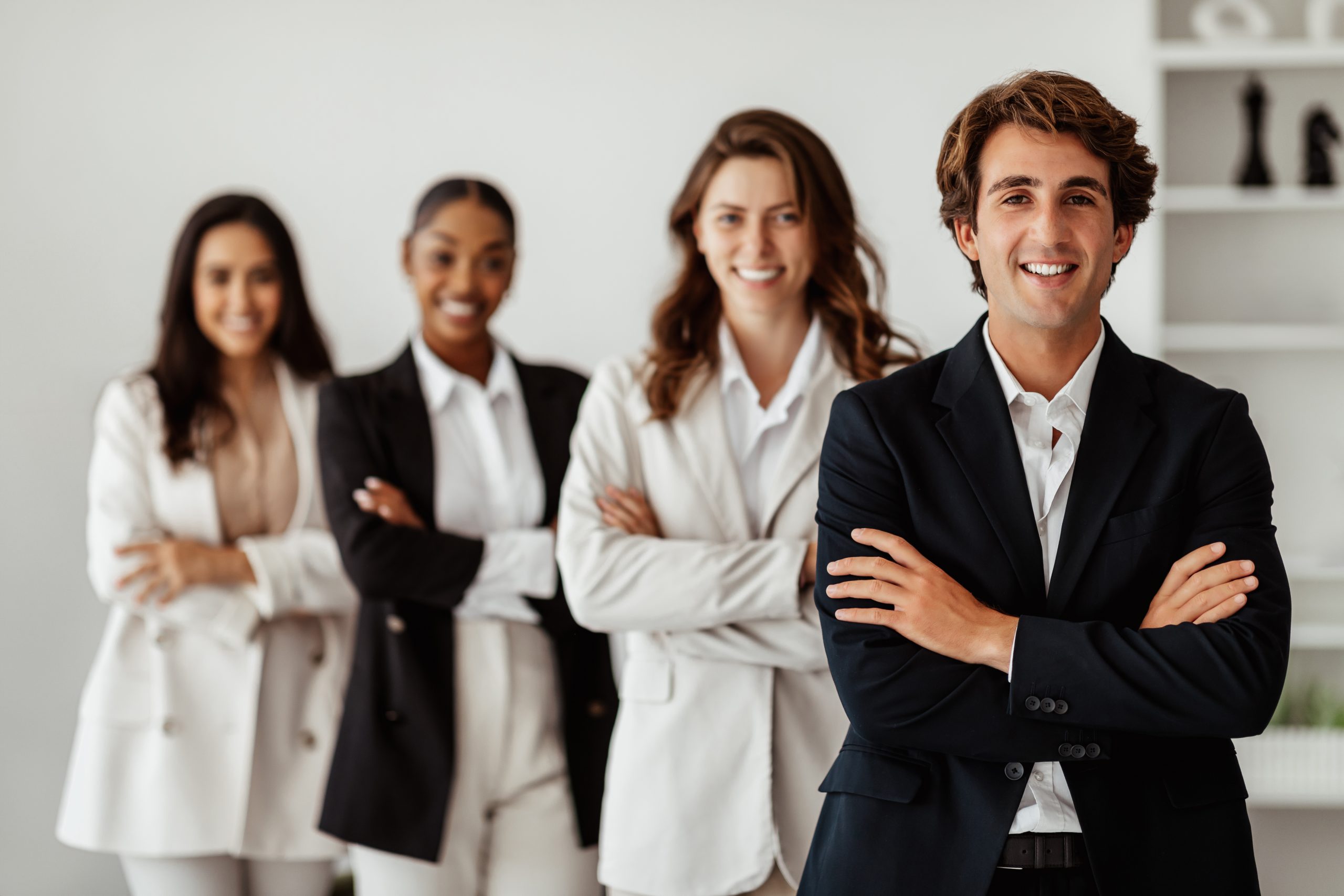 Four professionally dressed people stand in a row with arms crossed, smiling, in an office setting—ready to assist clients with the NDIS Provider Portal.