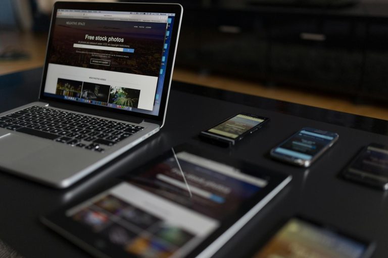 A laptop, tablet, and multiple smartphones displaying websites are arranged on a black table.