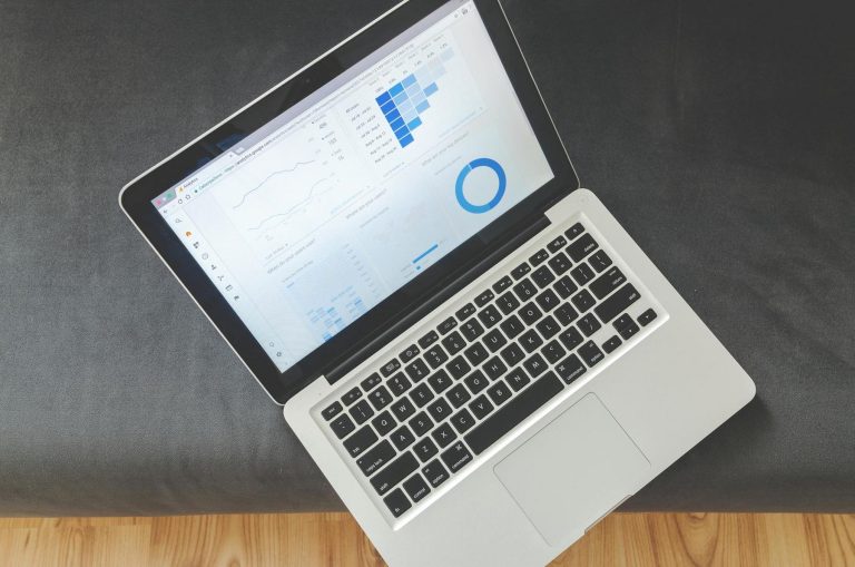 A laptop on a dark surface displays data analytics with charts and graphs on its screen.
