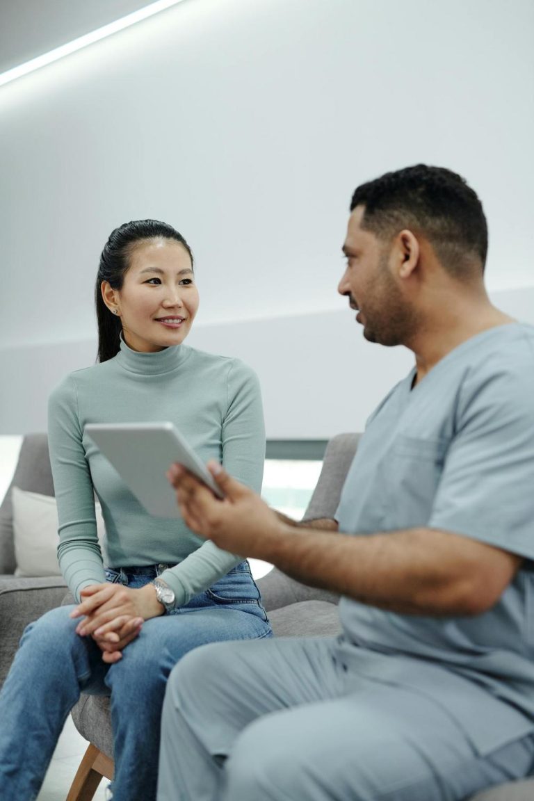 A healthcare professional shows a tablet to a seated woman during a consultation in a modern office setting.