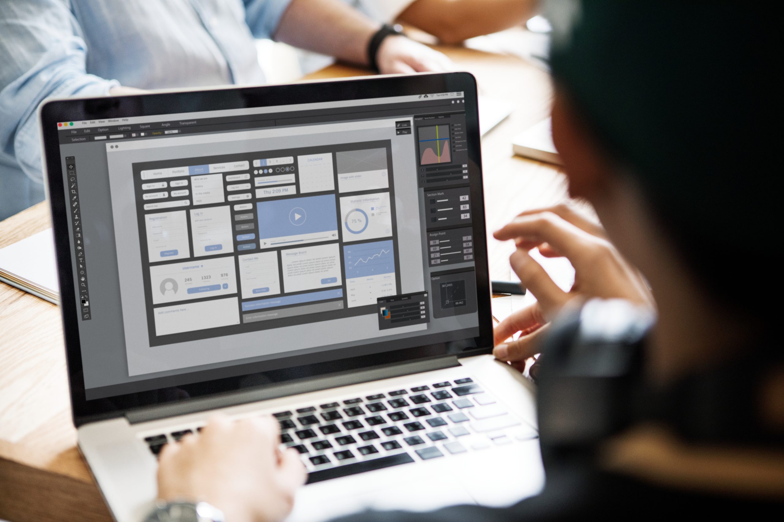 Person working on a laptop displaying a website wireframe with various UI elements and graphs, suggesting web design or development activity.
