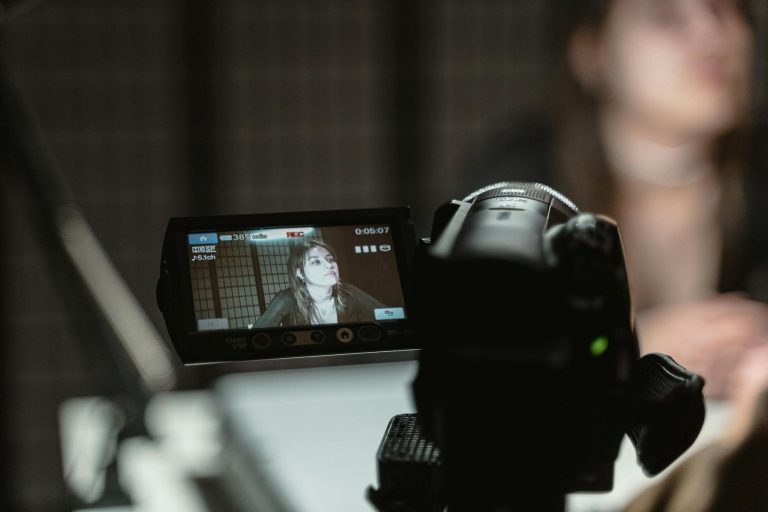 Close-up of a camera screen showing a woman being recorded, with the woman blurred in the background behind the camera.
